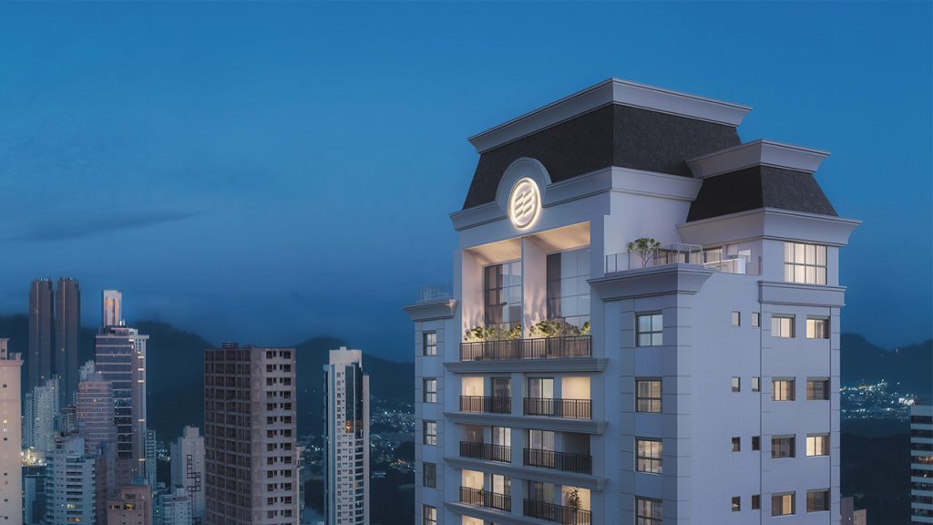 Fachada de edifício clássico ao anoitecer com cobertura tipo mansarda, sacadas com iluminação amarelada e vista parcial de outros prédios e morros ao longe.