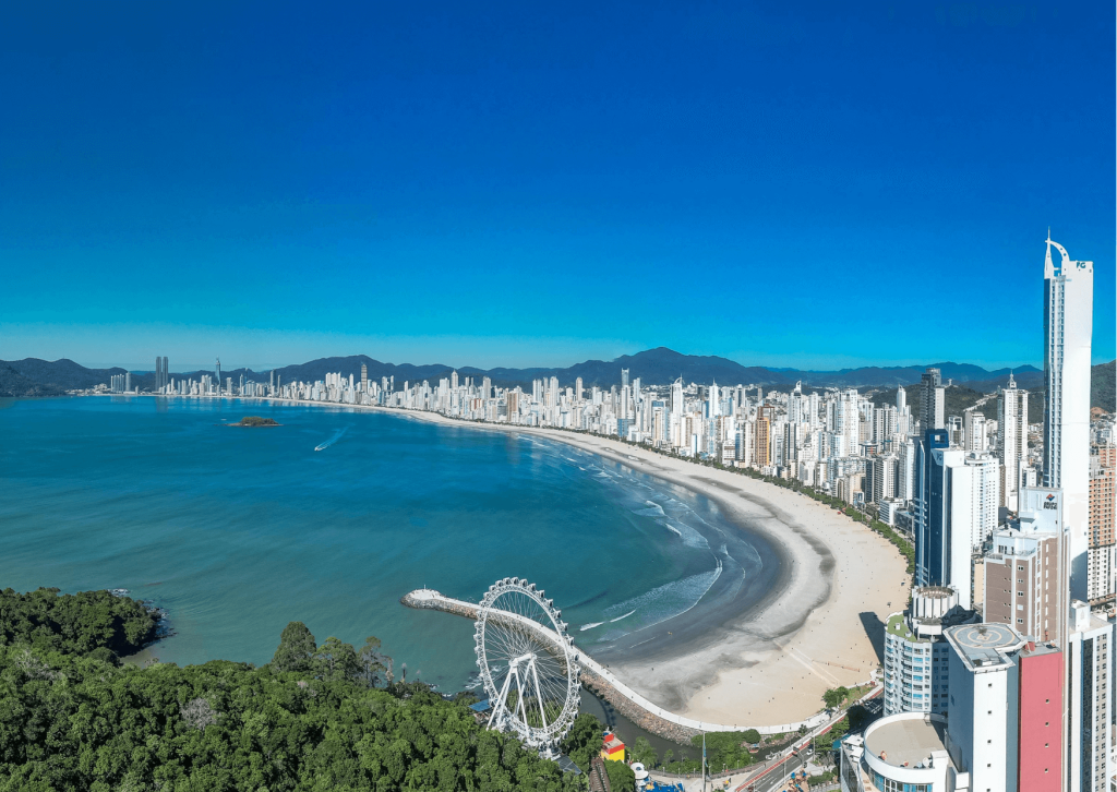 Roda-gigante Big Wheel na Barra Norte de Balneário Camboriú vista de cima, com orla curva, praia extensa, mar azul e skyline de arranha-céus ao fundo.
