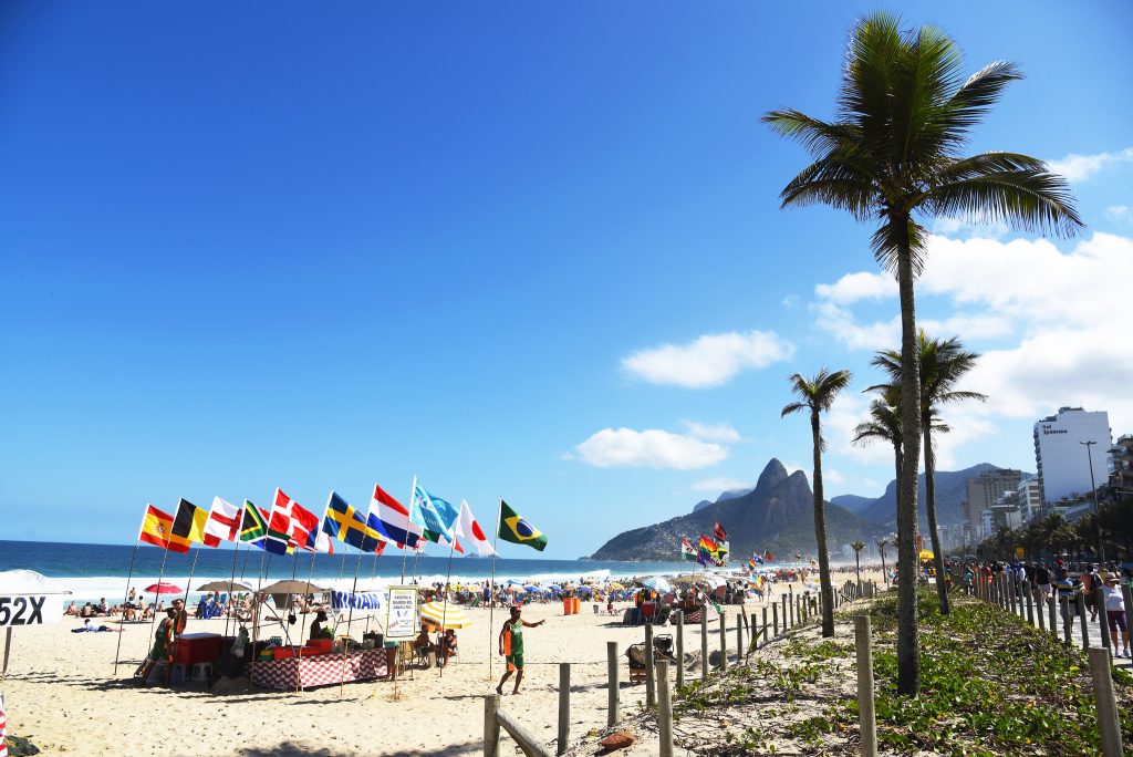 Orla da Praia de Ipanema no Rio de Janeiro (RJ) com bandeiras de vários países, palmeiras e o Morro Dois Irmãos ao fundo