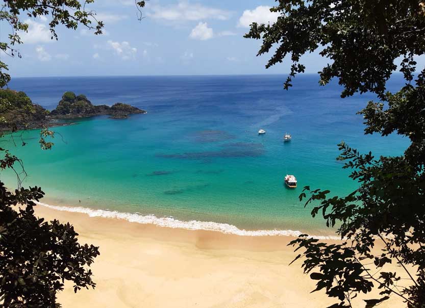 Turistas na Praia da Sepultura em Bombinhas (SC), com quiosques coloridos, guarda-sóis e águas calmas