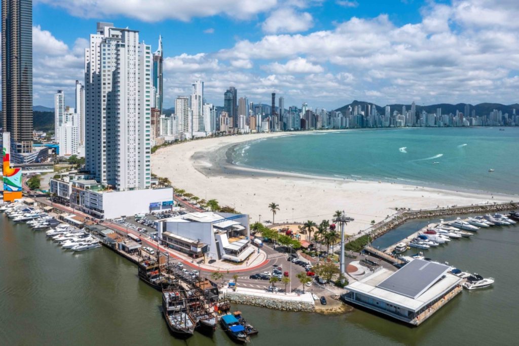 Vista aérea do Molhe da Barra Sul em Balneário Camboriú com um barco pirata ancorado no píer e arranha-céus ao fundo