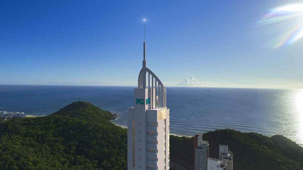 Renderização promocional da torre Pinnacle do FG Blue Coast erguendo-se acima de um morro florestado, com vista para o horizonte do oceano sob um céu claro e ensolarado.