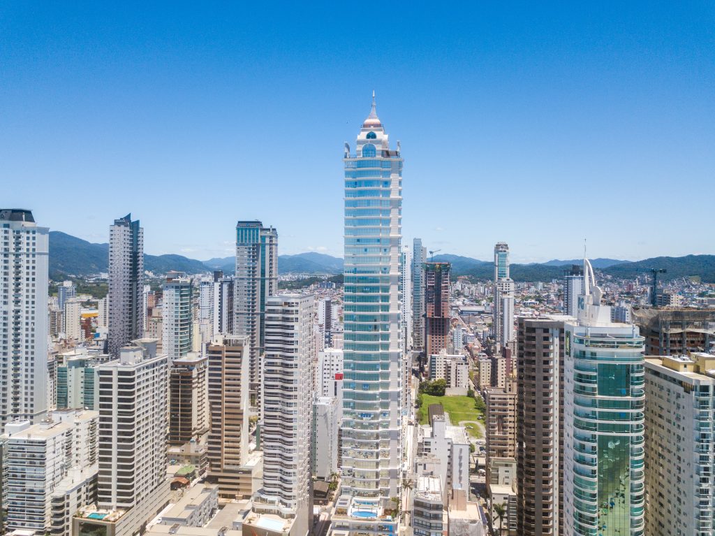 Edifício Millennium Palace em Balneário Camboriú com pináculo clássico, fachada de vidro azulado e frisos claros em cada andar