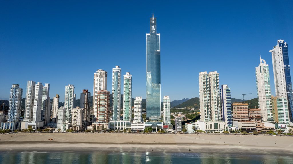 Edifício One Tower (FG Tower) em Balneário Camboriú com fachada envidraçada escura, faixas brancas horizontais e logo FG no topo