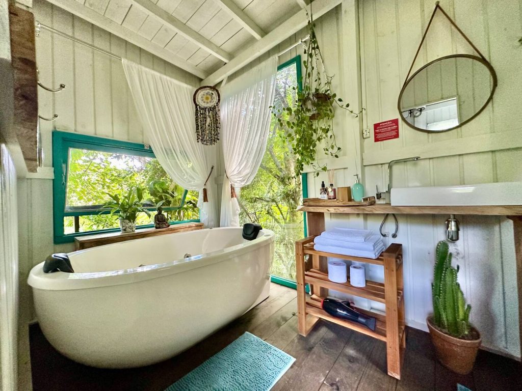 Banheira de hidromassagem em banheiro de chalé com interior em madeira e vista para a mata