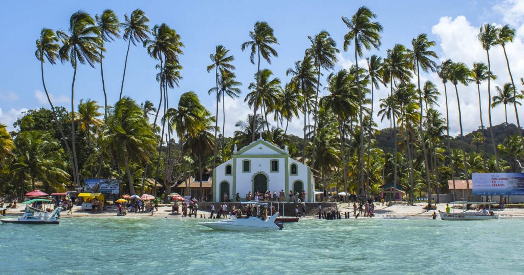 Igreja de São Benedito à beira-mar na Praia dos Carneiros (PE), cercada por coqueiros altos e águas calmas