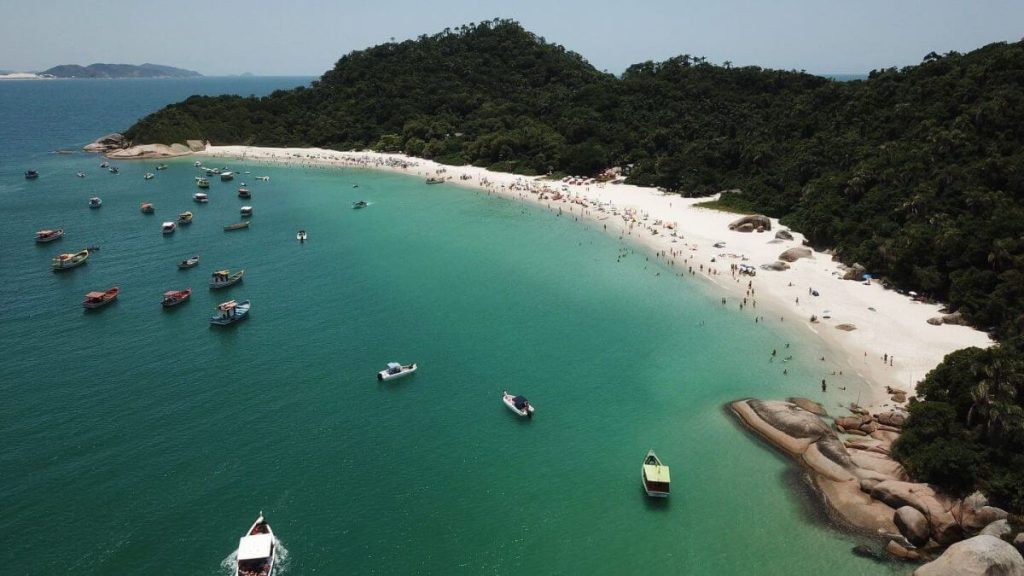 Panorâmica da Ilha do Campeche em Florianópolis (SC), destacando areia branca, águas cristalinas e barcos ancorados