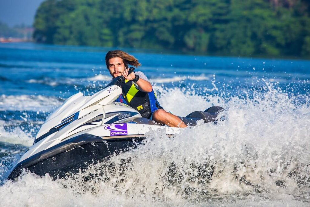 Homem de costas pilotando um pequeno barco motorizado em águas calmas durante o pôr do sol