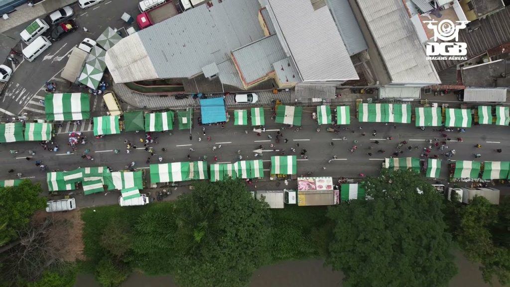 Vista aérea da Feirinha da Avenida Brasil em Balneário Camboriú, com barracas verdes e brancas alinhadas na rua e pedestres circulando