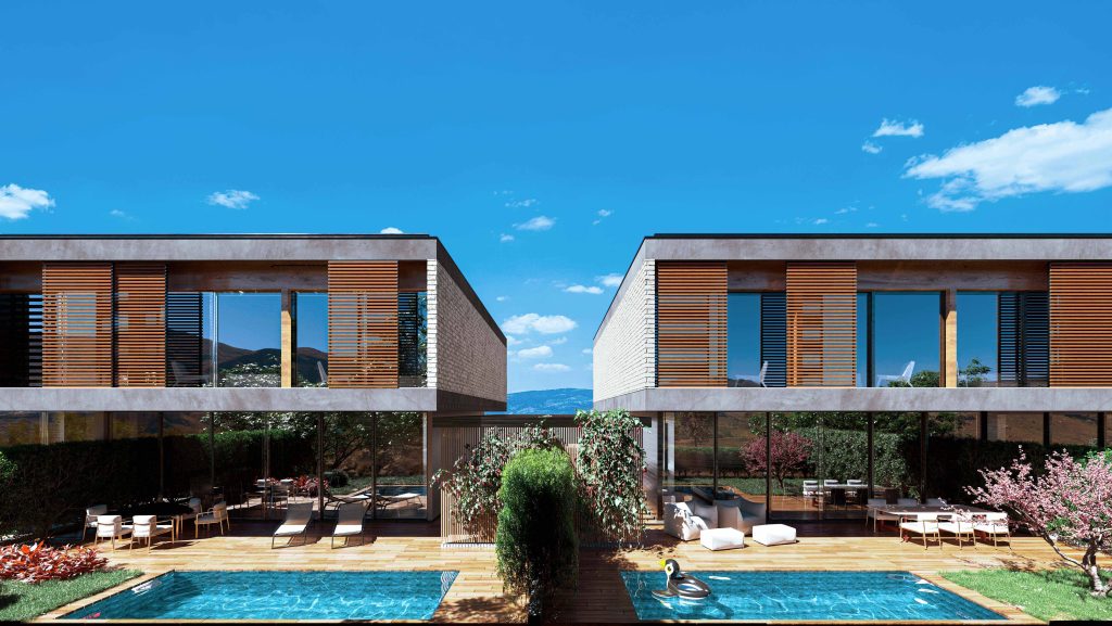 Duas casas modernas em concreto e madeira, unidas por deck com piscina, rodeadas por vegetação e montanhas ao fundo.