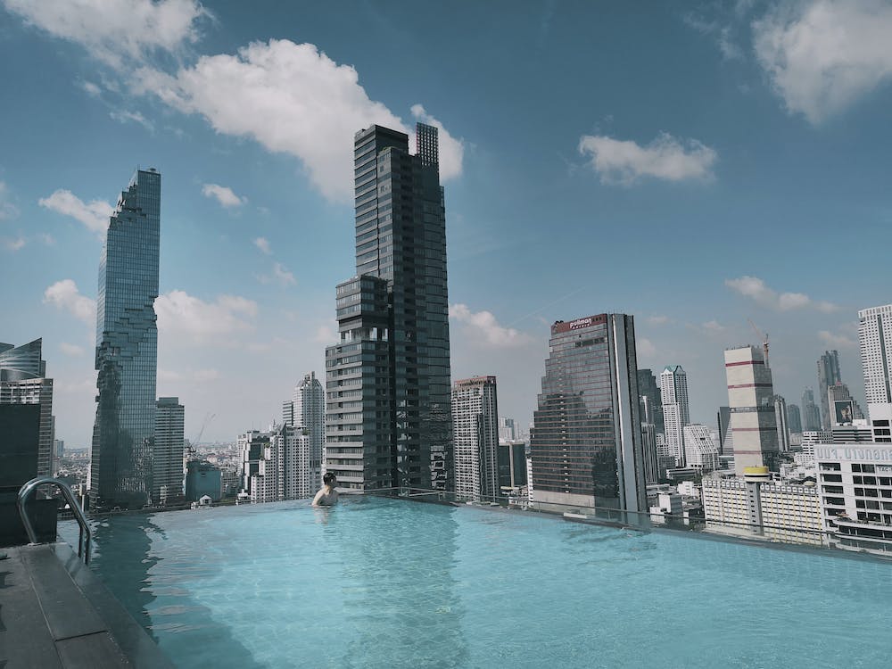Piscina de borda infinita em rooftop durante o dia, com vista para arranha-céus sob céu azul