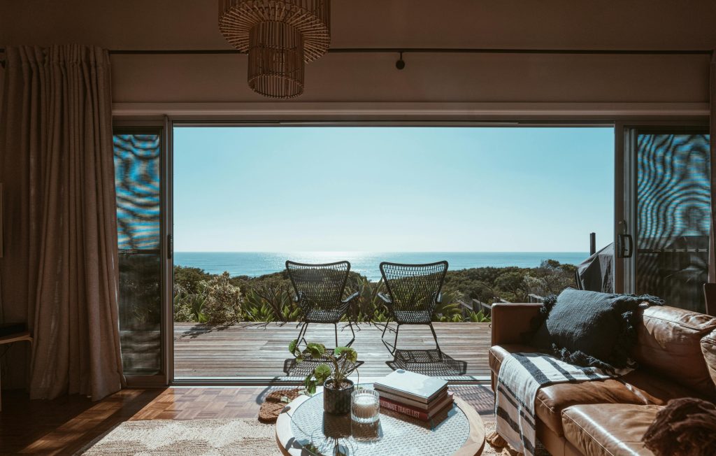 Sala de estar de chalé com portas de vidro que se abrem para deck de madeira e vista para o mar