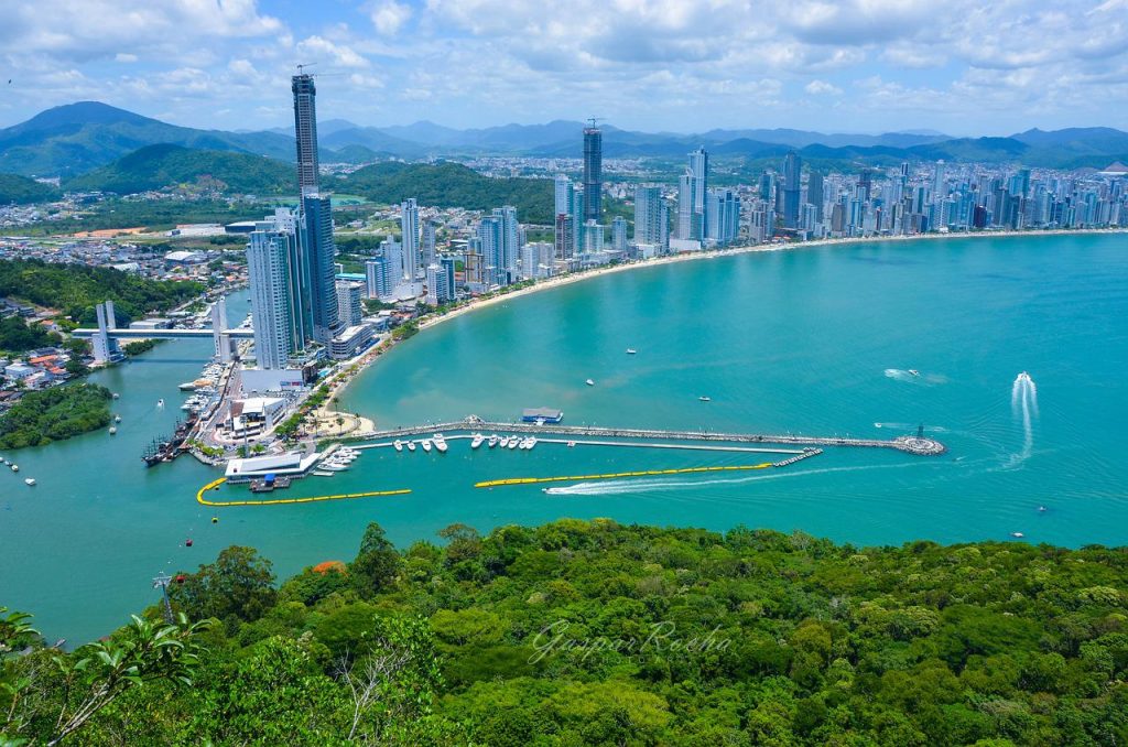Panorâmica de Balneário Camboriú vista do Morro do Careca, mostrando pier, prédios altos e mata atlântica em primeiro plano