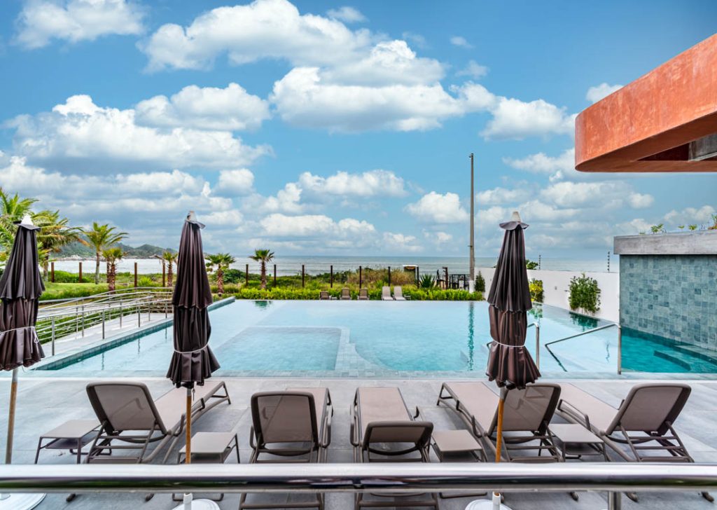 Piscina de borda infinita com espreguiçadeiras e guarda-sóis, de frente para o mar e o horizonte.